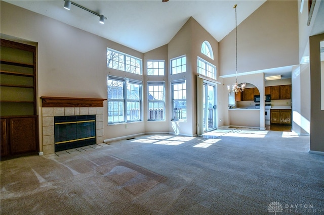 unfurnished living room featuring track lighting, carpet floors, an inviting chandelier, baseboards, and a tile fireplace