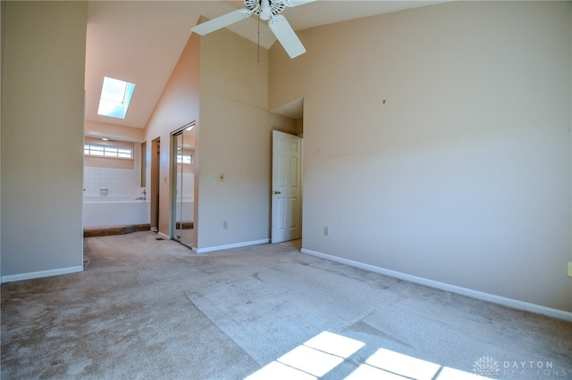 carpeted empty room featuring a skylight, a ceiling fan, baseboards, and high vaulted ceiling