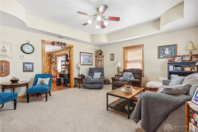 carpeted living room with a raised ceiling, plenty of natural light, ceiling fan, and a textured ceiling