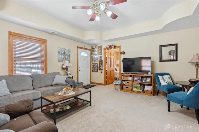 living room featuring a tray ceiling, a ceiling fan, baseboards, and light carpet