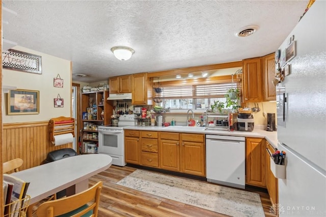 kitchen featuring white appliances, visible vents, a sink, under cabinet range hood, and wainscoting