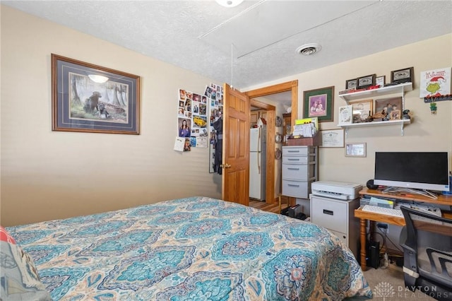 bedroom featuring visible vents, a textured ceiling, freestanding refrigerator, carpet, and attic access