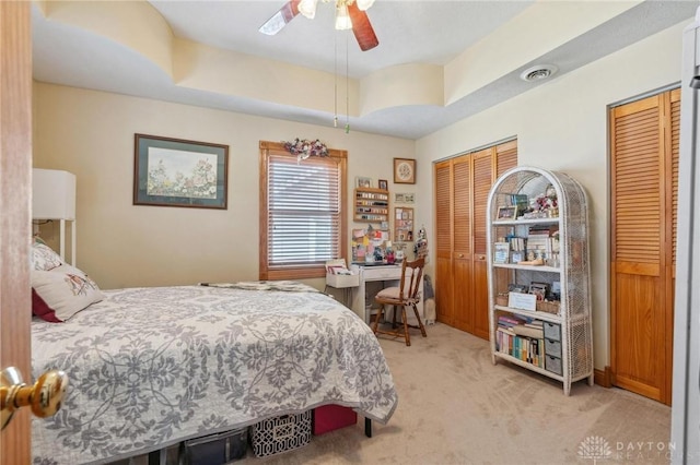 bedroom with visible vents, light colored carpet, a ceiling fan, and multiple closets