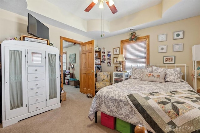 bedroom with a ceiling fan, a tray ceiling, and light colored carpet