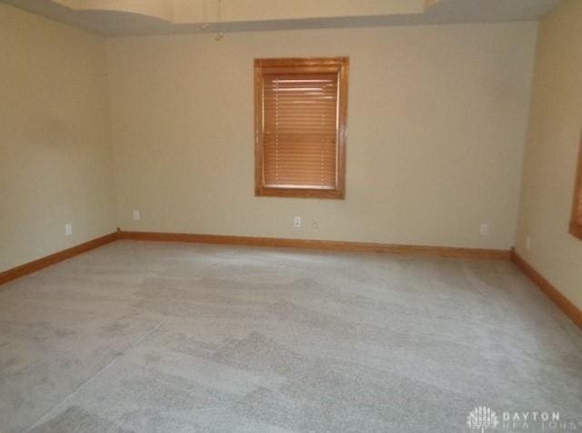 spare room with baseboards and light colored carpet