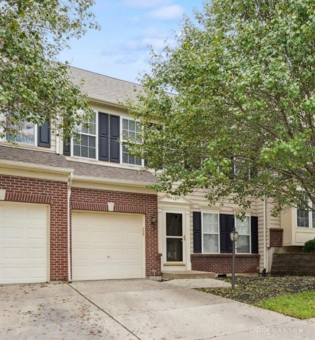 multi unit property featuring concrete driveway, an attached garage, brick siding, and roof with shingles