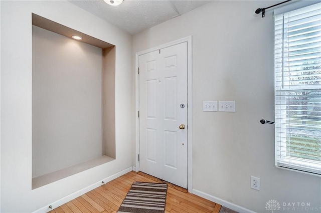 foyer featuring a textured ceiling, light wood-type flooring, and baseboards