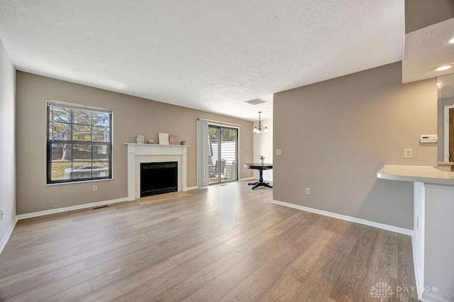 unfurnished living room with visible vents, a fireplace with flush hearth, a textured ceiling, wood finished floors, and baseboards