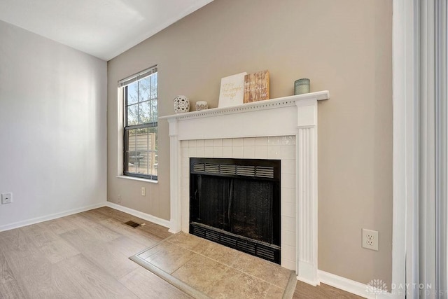 interior details with visible vents, baseboards, wood finished floors, and a tiled fireplace