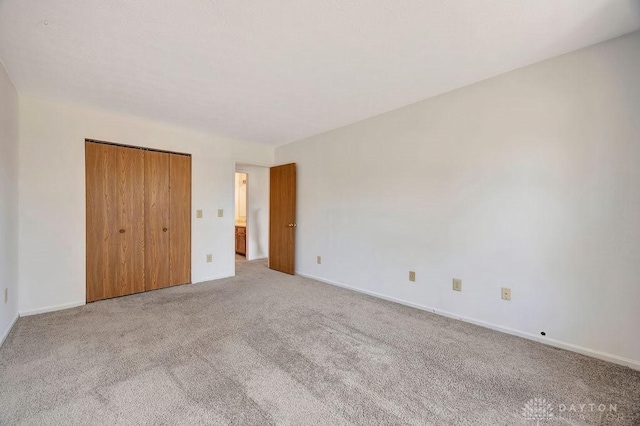 unfurnished bedroom with a closet, baseboards, and light colored carpet