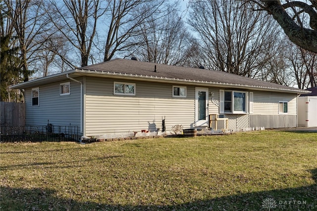 view of front of home with roof with shingles, a front yard, and fence