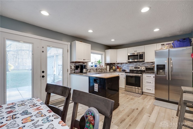 kitchen with a sink, backsplash, white cabinetry, appliances with stainless steel finishes, and light wood finished floors