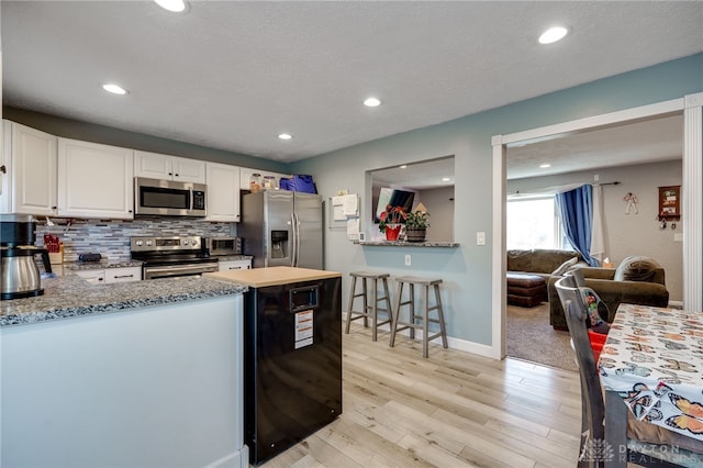 kitchen with light wood-type flooring, decorative backsplash, a peninsula, white cabinets, and stainless steel appliances