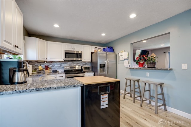 kitchen with baseboards, light wood finished floors, stainless steel appliances, white cabinets, and tasteful backsplash