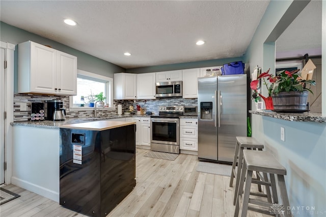 kitchen featuring tasteful backsplash, light wood finished floors, recessed lighting, appliances with stainless steel finishes, and white cabinetry