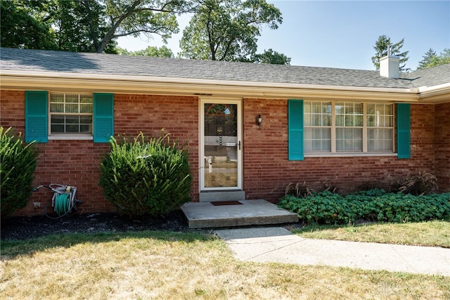 entrance to property featuring brick siding, a chimney, and a lawn