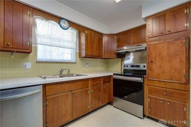 kitchen with under cabinet range hood, a sink, stainless steel appliances, decorative backsplash, and light floors