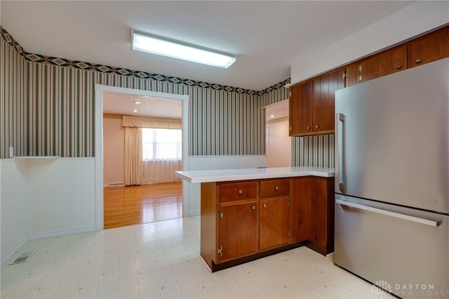 kitchen with a wainscoted wall, freestanding refrigerator, a peninsula, wallpapered walls, and light countertops