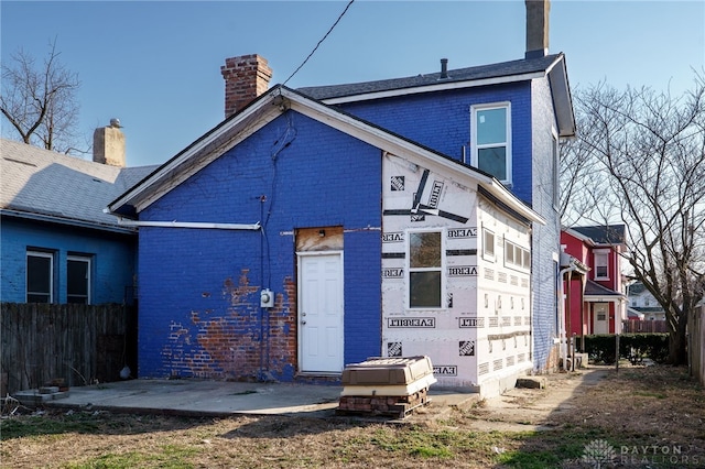 back of house with brick siding, a chimney, and fence