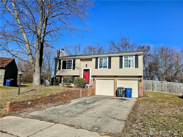 split foyer home featuring brick siding, fence, aphalt driveway, a chimney, and an attached garage