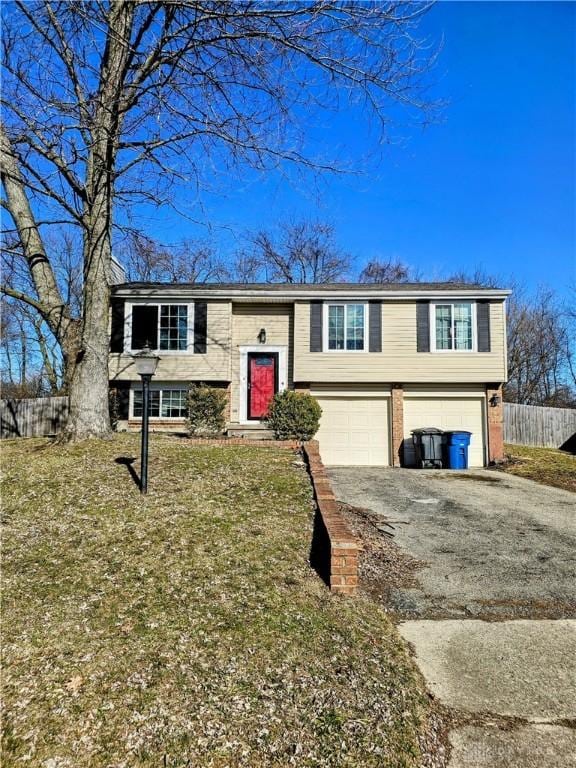 raised ranch with brick siding, driveway, a garage, and fence