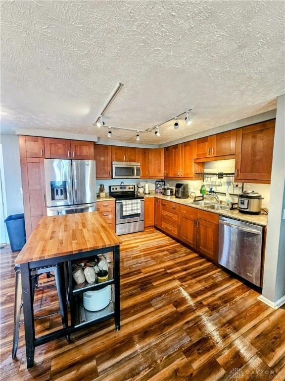 kitchen featuring dark wood-type flooring, wood counters, a textured ceiling, appliances with stainless steel finishes, and brown cabinetry