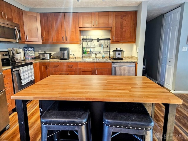 kitchen featuring a breakfast bar area, a sink, appliances with stainless steel finishes, brown cabinets, and butcher block counters