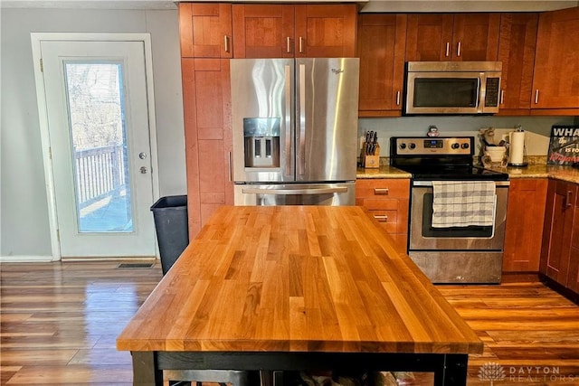 kitchen featuring dark wood finished floors, brown cabinetry, appliances with stainless steel finishes, and wood counters