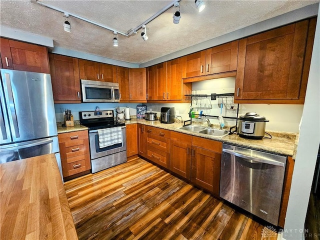 kitchen with a sink, a textured ceiling, appliances with stainless steel finishes, light countertops, and dark wood-style flooring