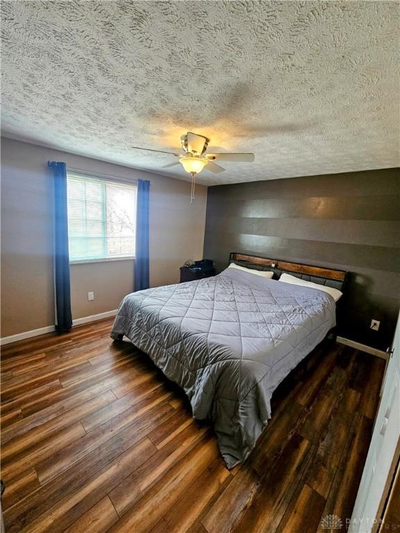 bedroom with ceiling fan, a textured ceiling, baseboards, and wood finished floors