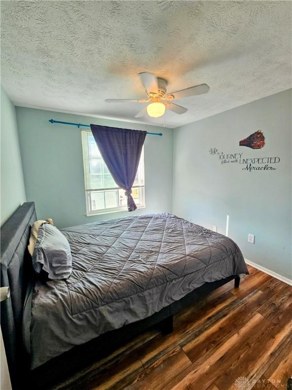 bedroom featuring baseboards, a textured ceiling, wood finished floors, and a ceiling fan