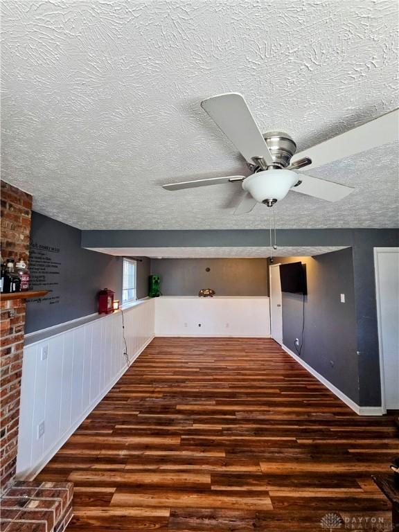 interior space featuring a ceiling fan, a textured ceiling, wood finished floors, and wainscoting