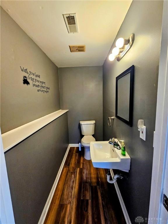 bathroom featuring toilet, wood finished floors, visible vents, and a sink