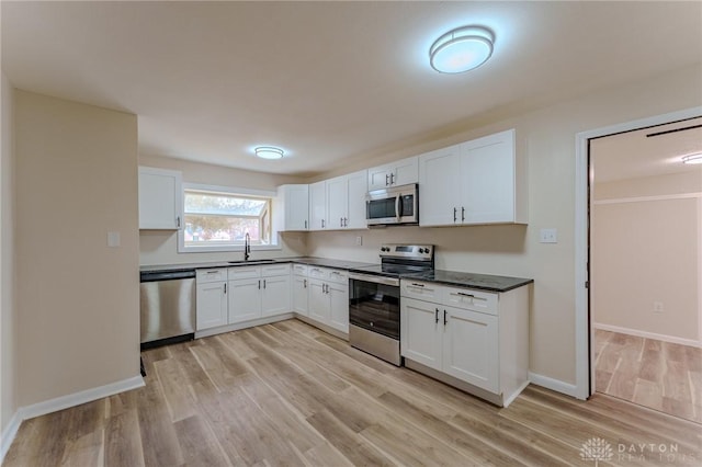 kitchen featuring light wood-type flooring, a sink, dark countertops, appliances with stainless steel finishes, and white cabinets