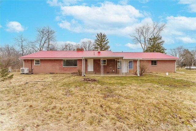 rear view of property with a lawn, brick siding, and metal roof