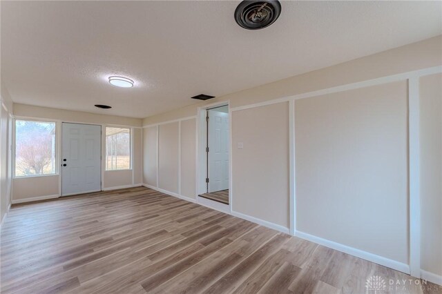 empty room with baseboards, visible vents, light wood-type flooring, and a textured ceiling