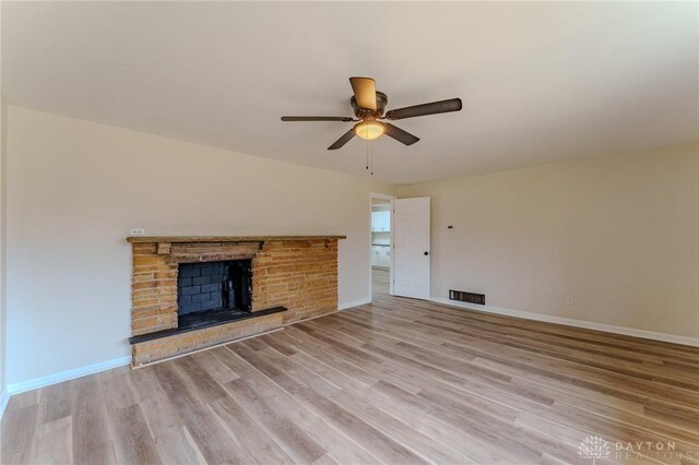 unfurnished living room with visible vents, a brick fireplace, baseboards, ceiling fan, and wood finished floors