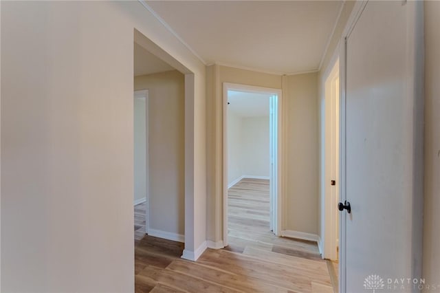 hall featuring light wood finished floors, crown molding, and baseboards