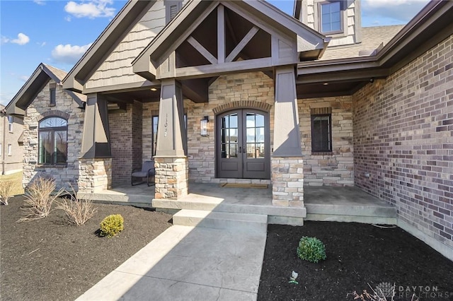 entrance to property featuring a porch, stone siding, and french doors