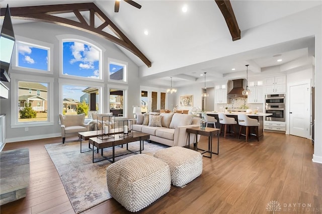 living area featuring baseboards, beam ceiling, hardwood / wood-style flooring, high vaulted ceiling, and a ceiling fan