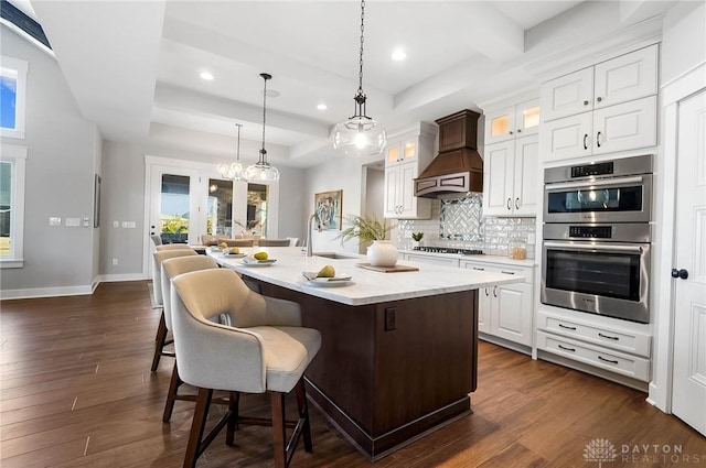 kitchen featuring custom range hood, a sink, tasteful backsplash, double oven, and a raised ceiling