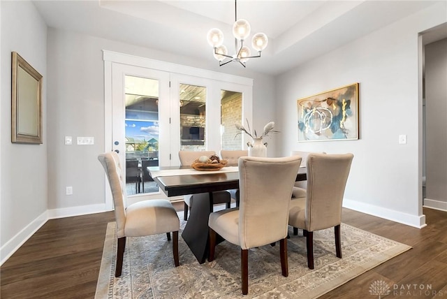 dining space with dark wood-style floors, an inviting chandelier, baseboards, and a tray ceiling