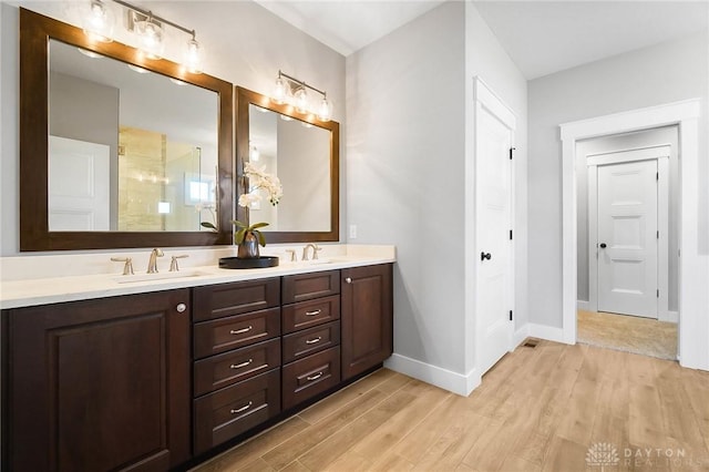 full bath featuring baseboards, double vanity, wood finished floors, a shower, and a sink