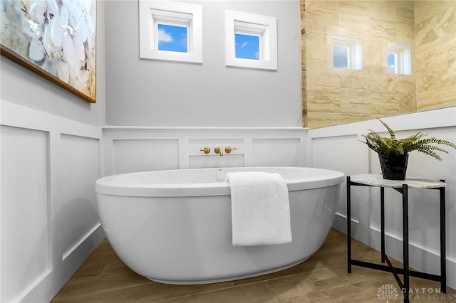 bathroom featuring a soaking tub, a decorative wall, a wainscoted wall, and wood tiled floor