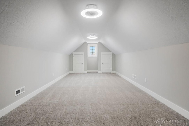 additional living space with baseboards, visible vents, lofted ceiling, a textured ceiling, and carpet flooring