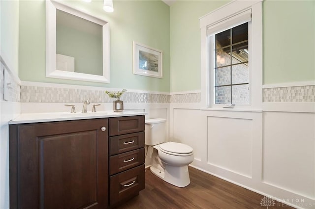 bathroom featuring vanity, toilet, wood finished floors, and wainscoting