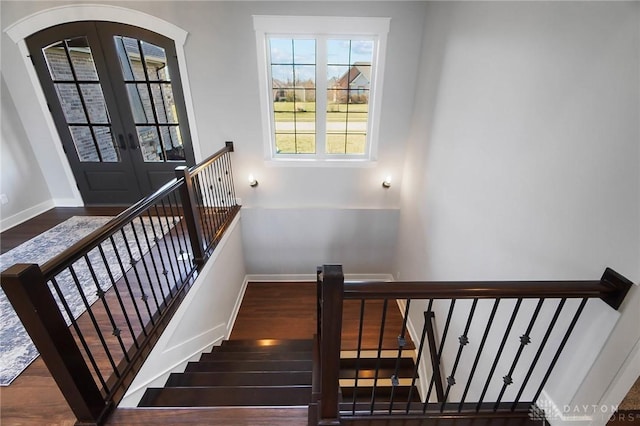 staircase with wood finished floors, french doors, arched walkways, and baseboards