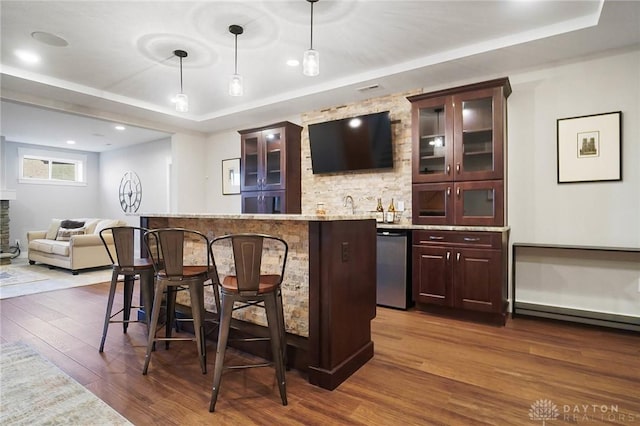 bar featuring dishwasher, a tray ceiling, hanging light fixtures, bar, and dark wood-style floors