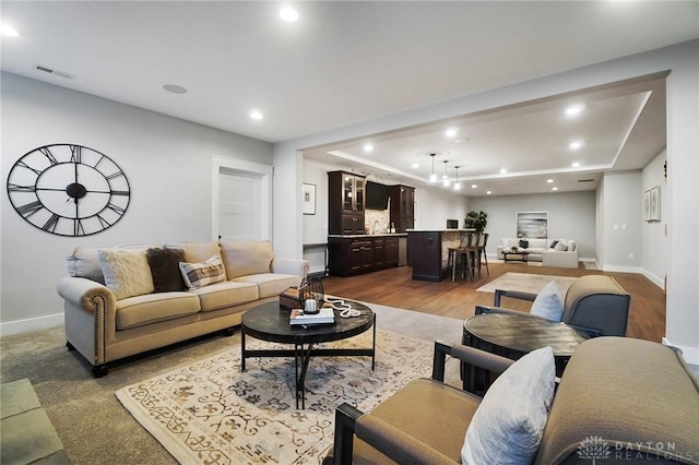 living room with visible vents, a raised ceiling, recessed lighting, baseboards, and indoor bar