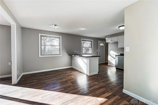 kitchen featuring dark countertops, dark wood-type flooring, baseboards, a peninsula, and white cabinetry